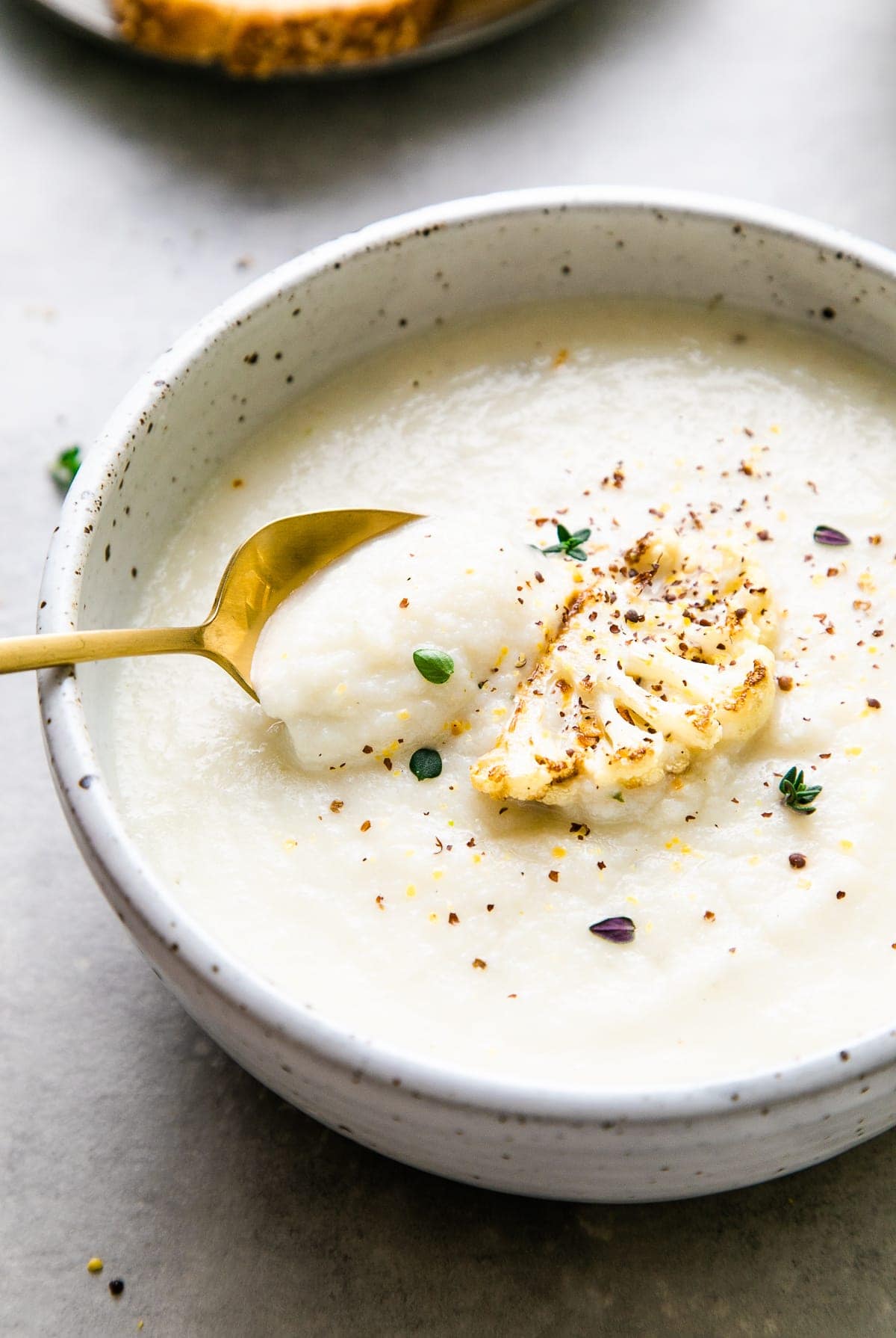 side angle view of creamy vegan cauliflower soup with spoon and items surrounding.