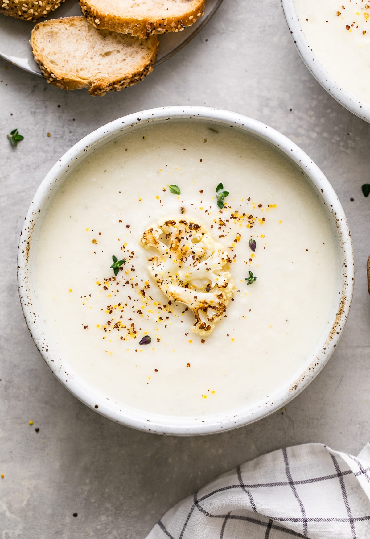 top down view of a bowl with a serving of creamy vegan cauliflower soup with items surrounding.