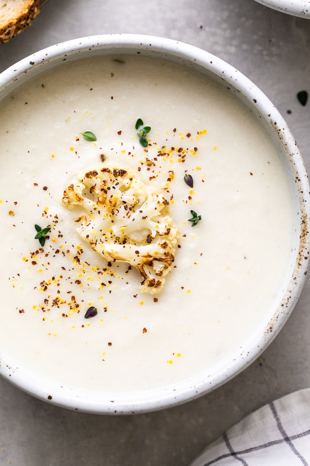 top down view of a bowl with a serving of creamy vegan cauliflower soup with items surrounding.