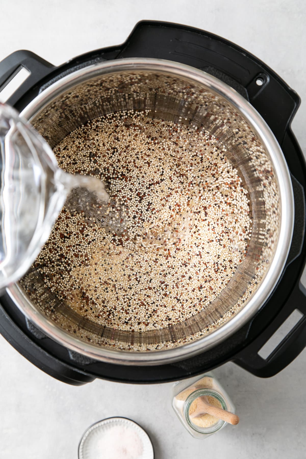 top down view showing the process of pouring water into instant pot with quinoa.