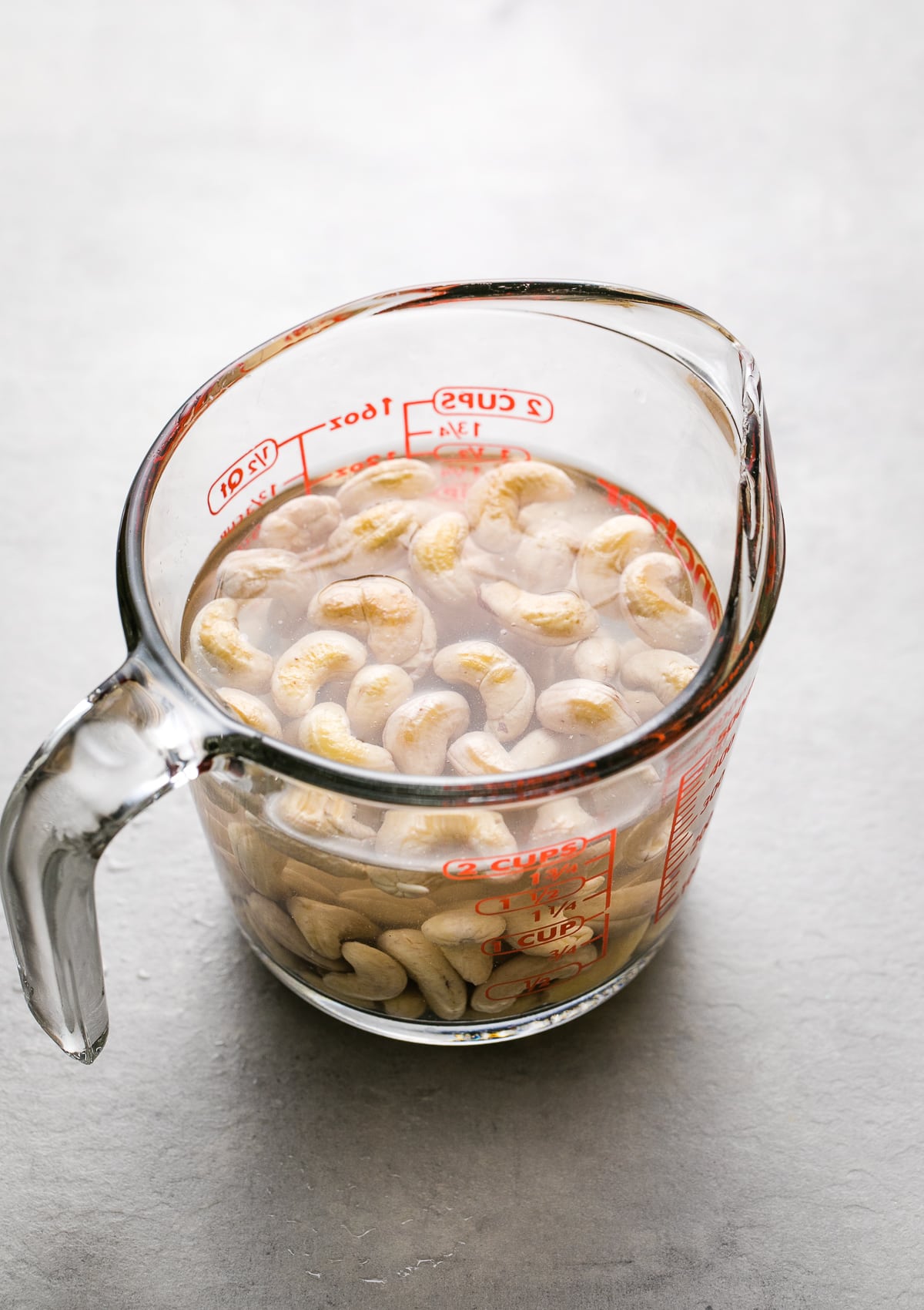 side angle view of cashews soaking in water in a glass measuring cup.