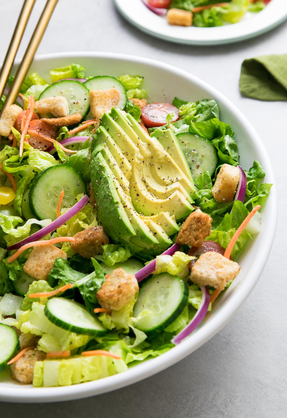 side angle view of house salad with apple cider vinaigrette and sliced avocado.