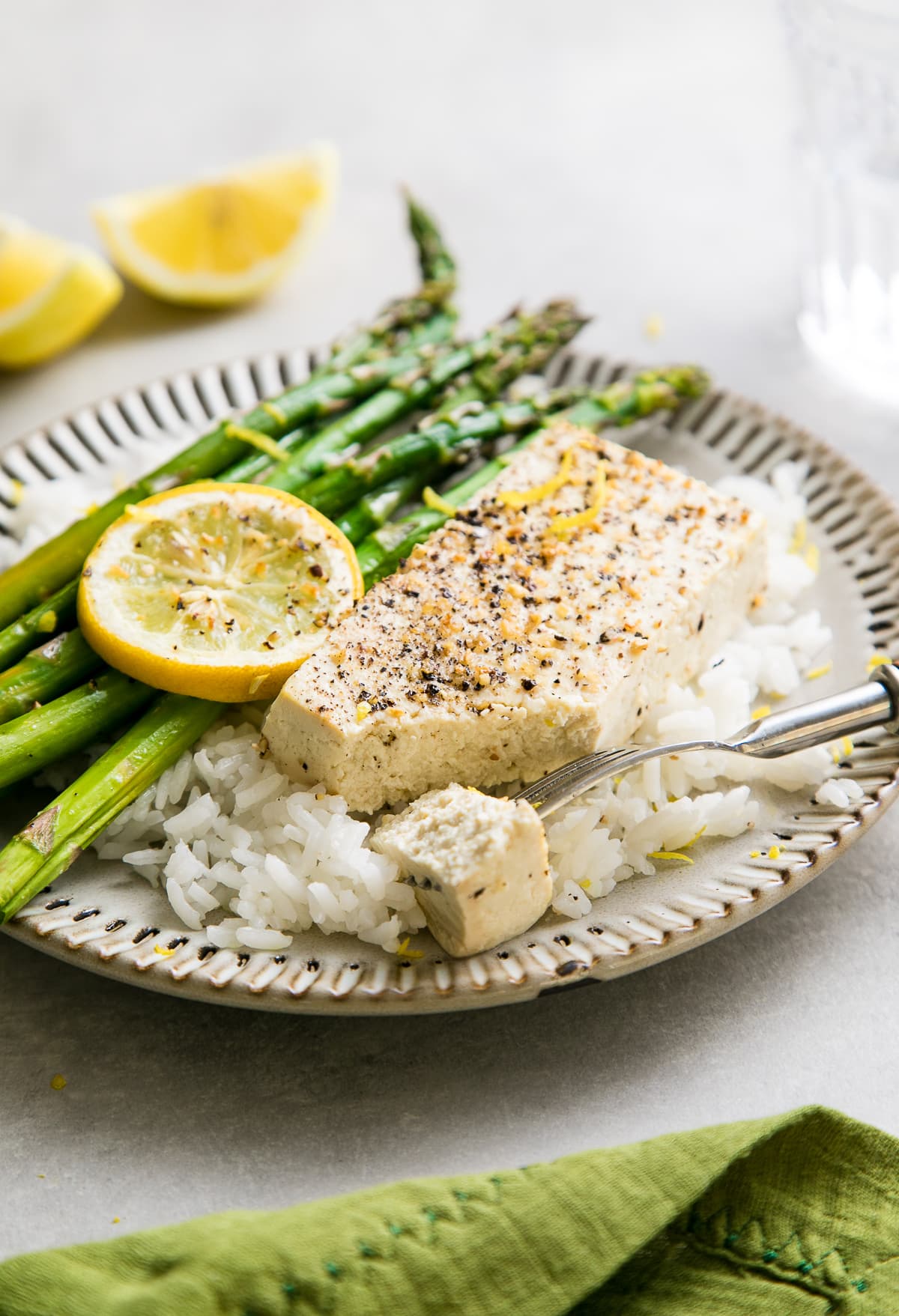 side angle view of baked lemon pepper tofu with asparagus and rice on a small plate.