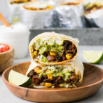 head on view of 2 halves of vegan burrito stacked on each other with items surrounding.