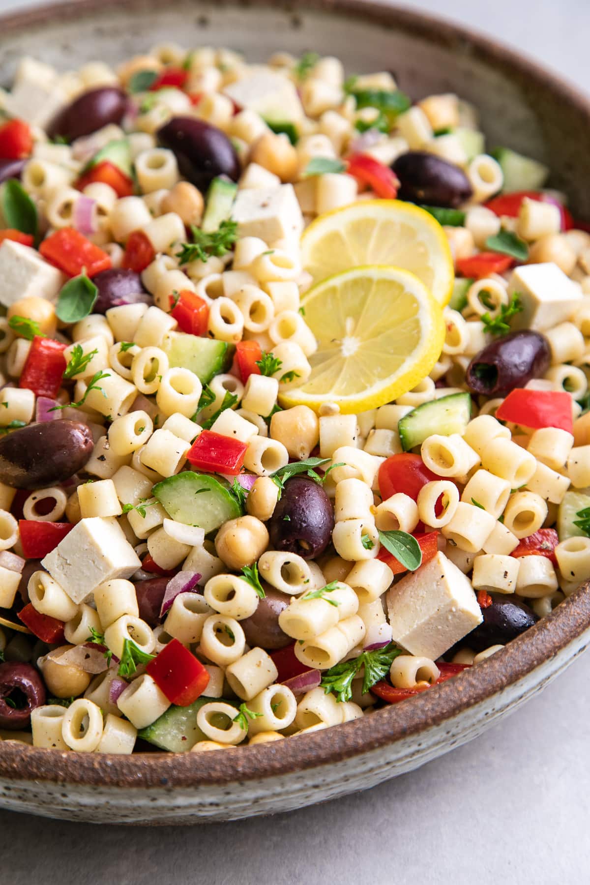 side angle view of healthy, vegan Greek pasta salad in a serving bowl with gold serving spoon.