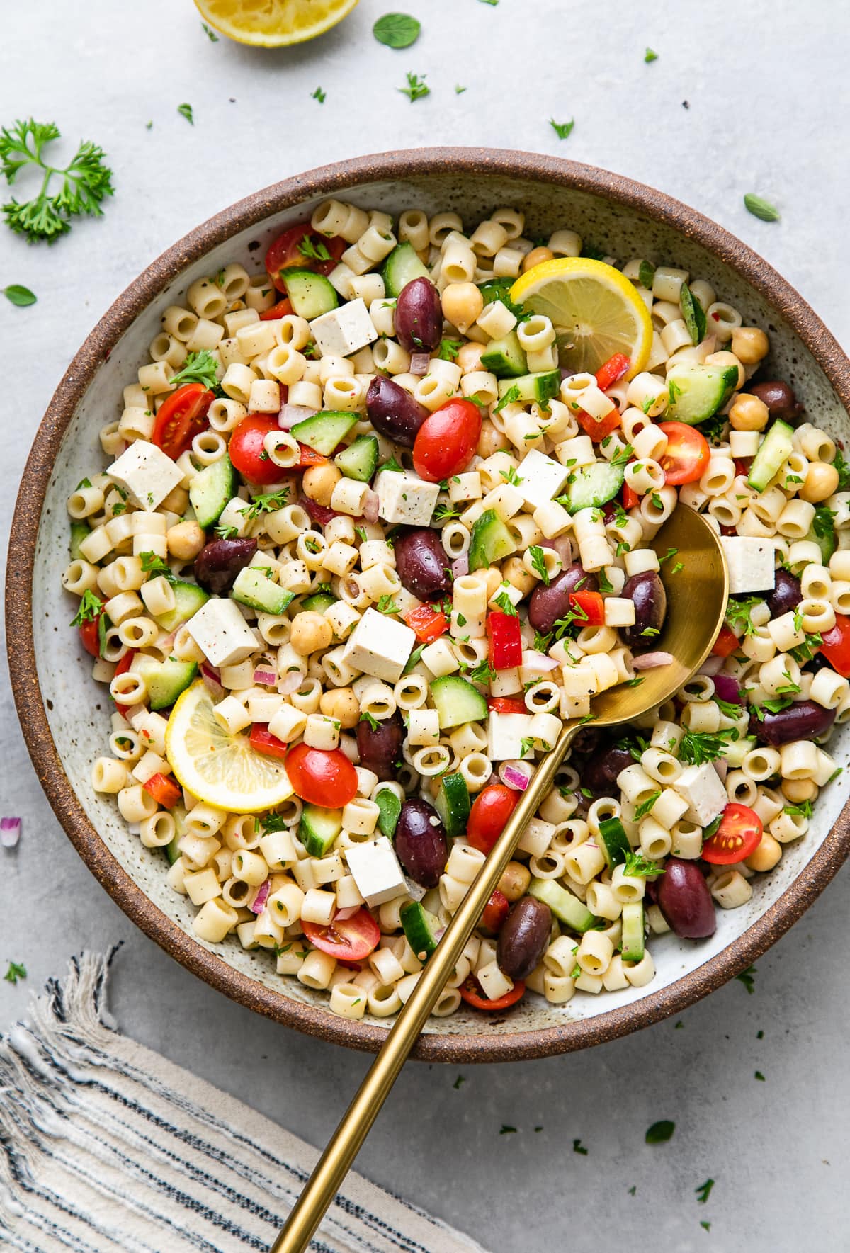 top down view of healthy, vegan Greek pasta salad in a serving bowl with gold serving spoon.