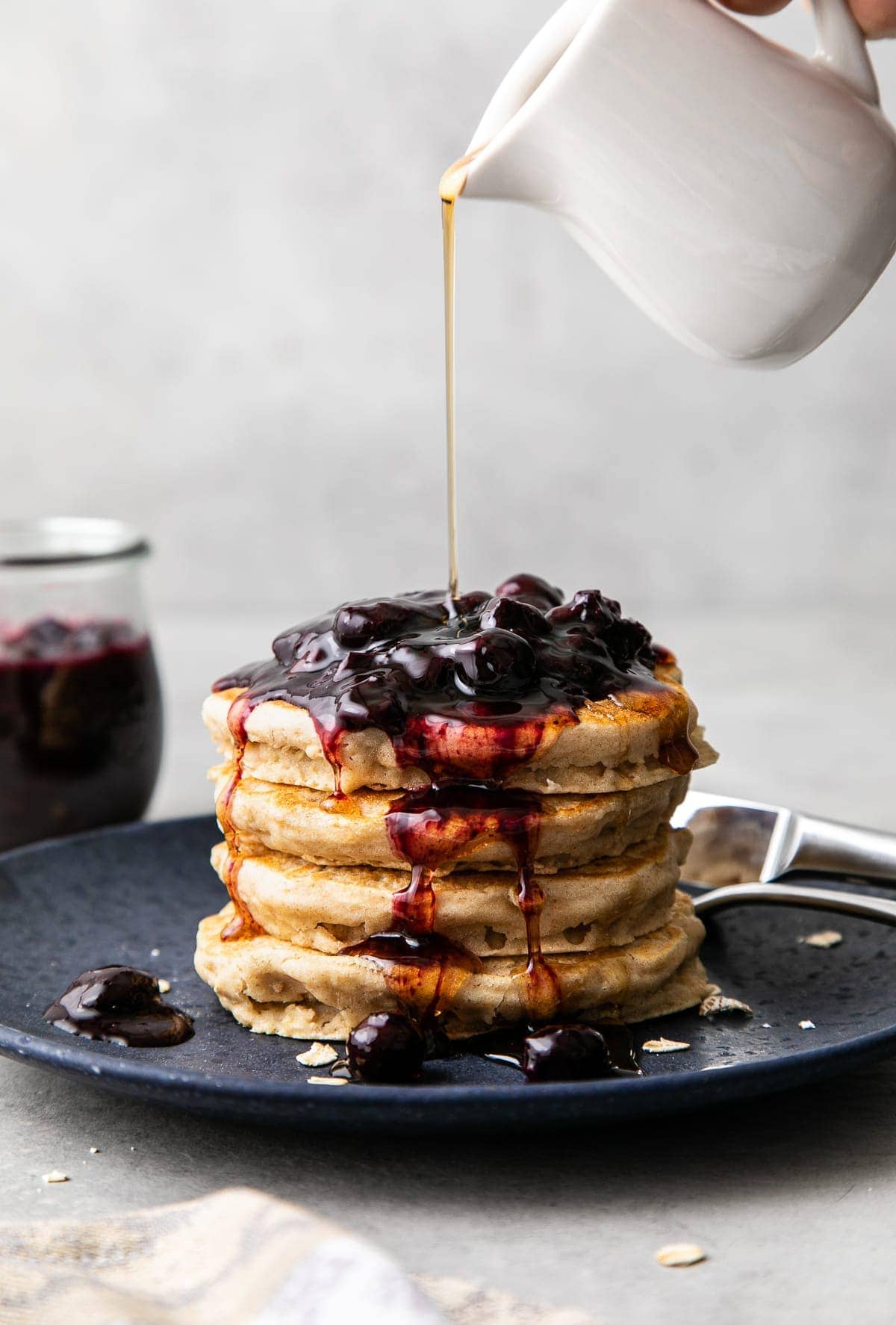 head on view of stacked pancakes with blueberry compote and being drizzled with syrup.