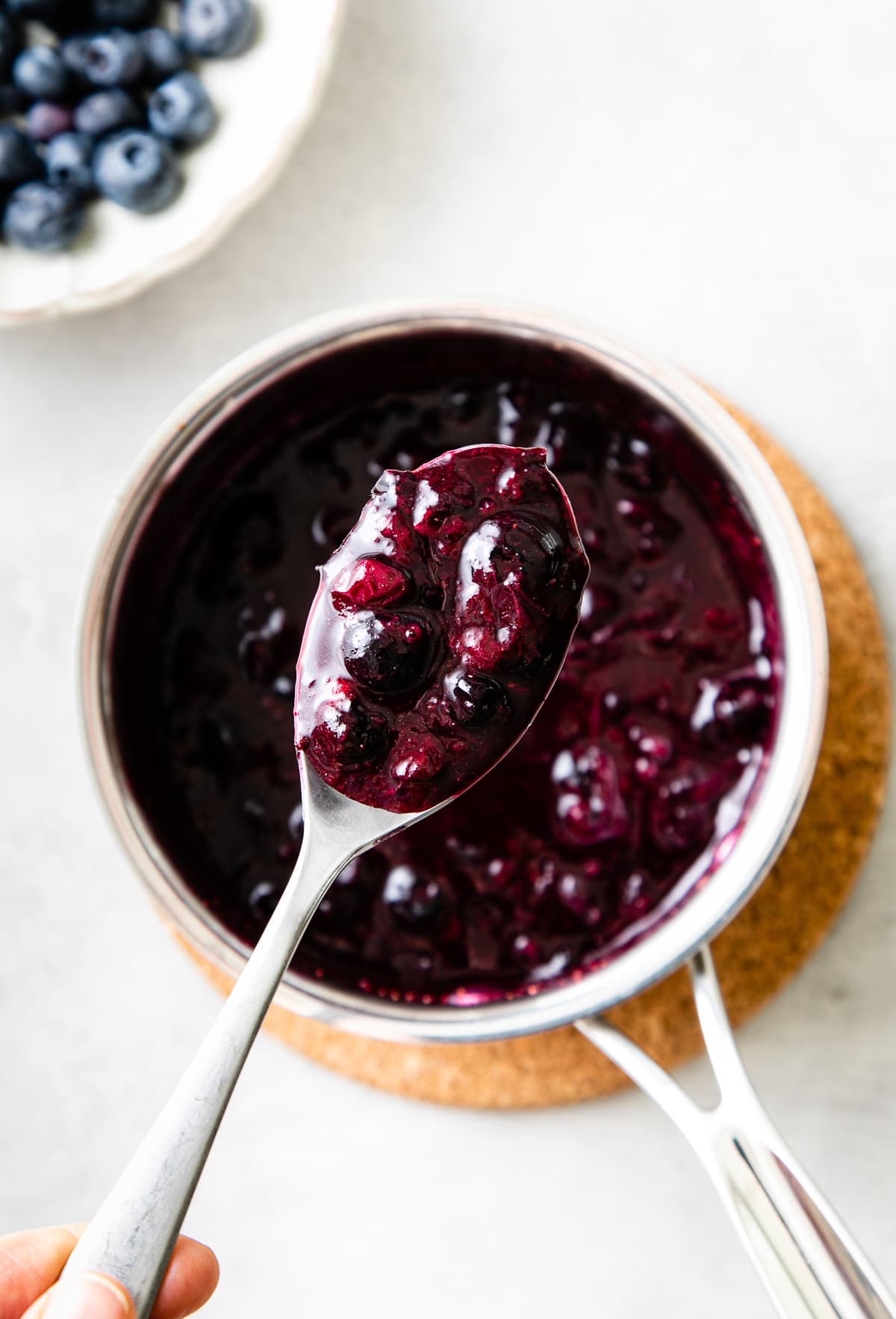 top down view of spoon holding scoop of blueberry compote over small pan with items surrounding.