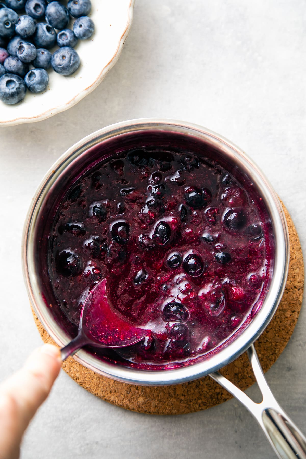 top down view showing the process of mashing blueberries in small pan.