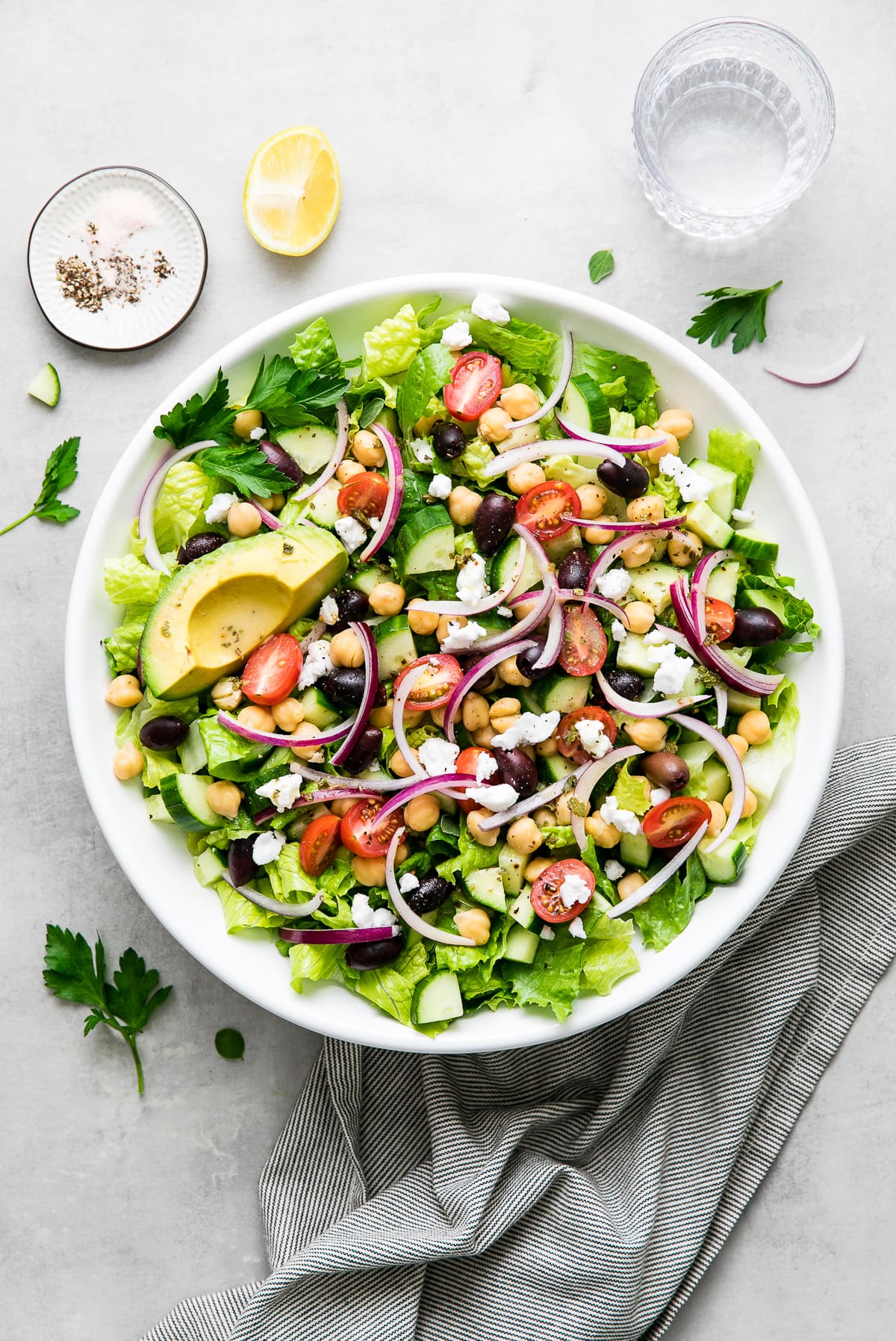 up close, top down view of mediterranean chop salad in a white bowl with items surrounding.