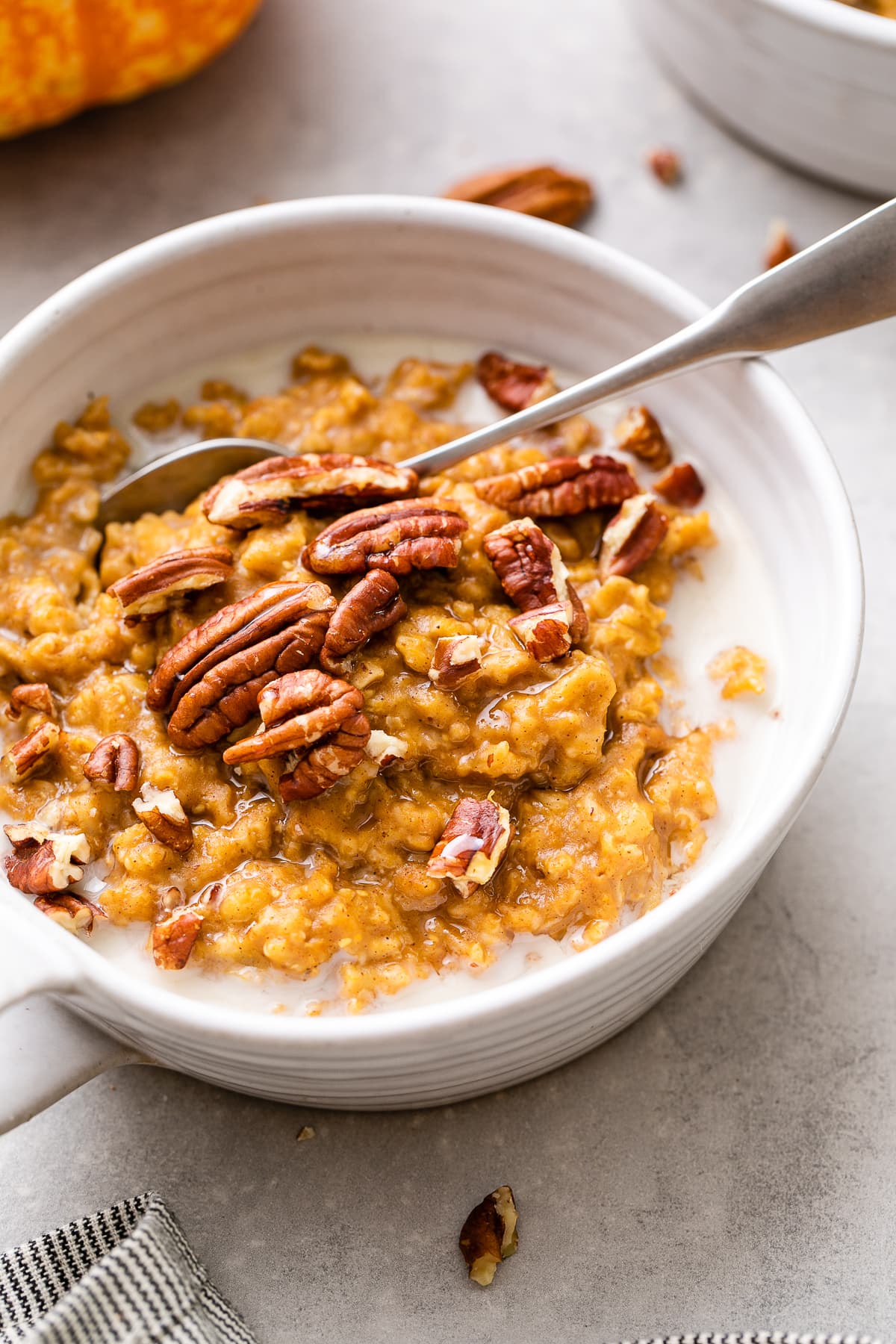 side angle view of vegan pumpkin oatmeal in a whole bowl with spoon and items surrounding.