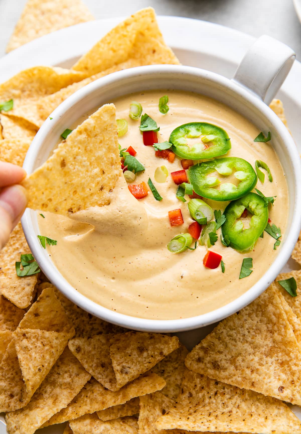 top down, side angle view of chip dipped into bowl of cashew vegan queso.