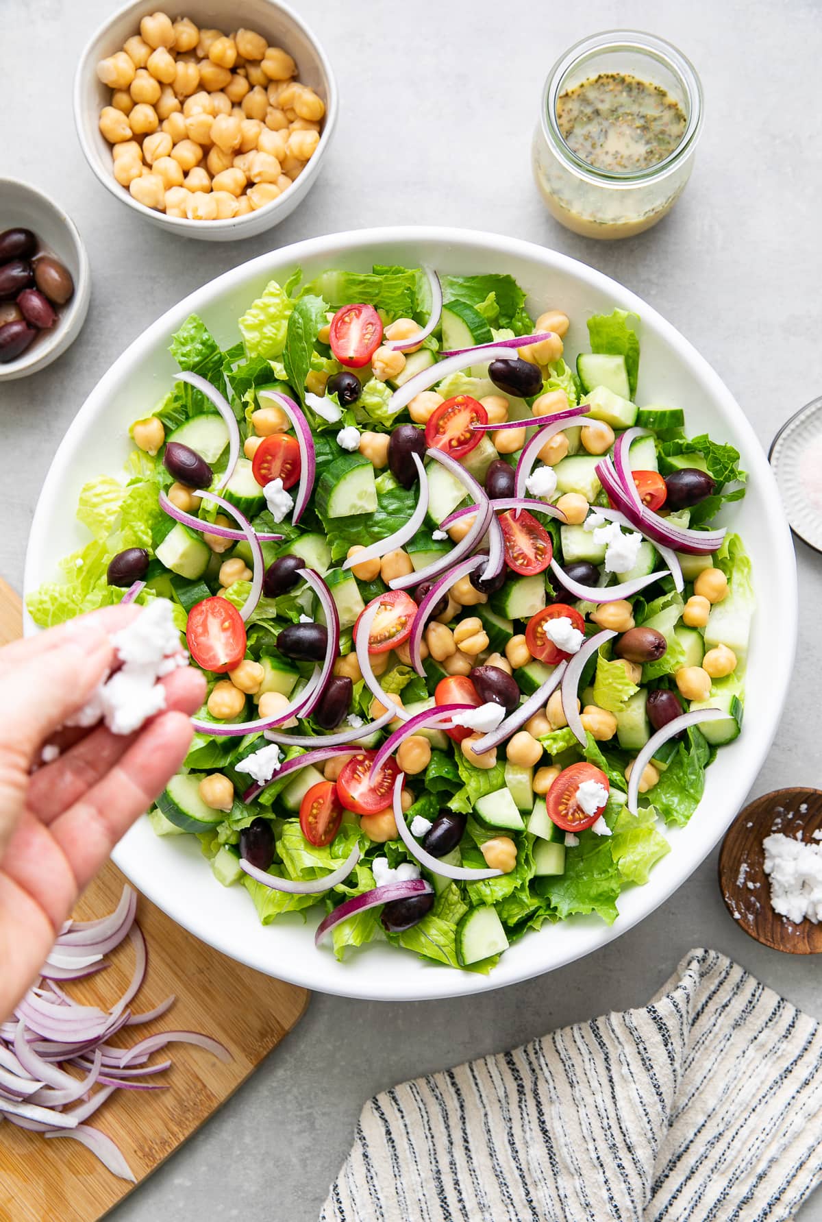 top down view showing the process of assembling mediterranean salad in a white bowl with items surrounding.