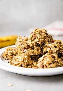 side angle view of group of stacked banana oatmeal chocolate chip cookies on a white plate with items surrounding.