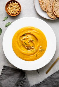 top down view of healthy vegan butternut squash and red lentil soup in a white bowl with items surrounding.
