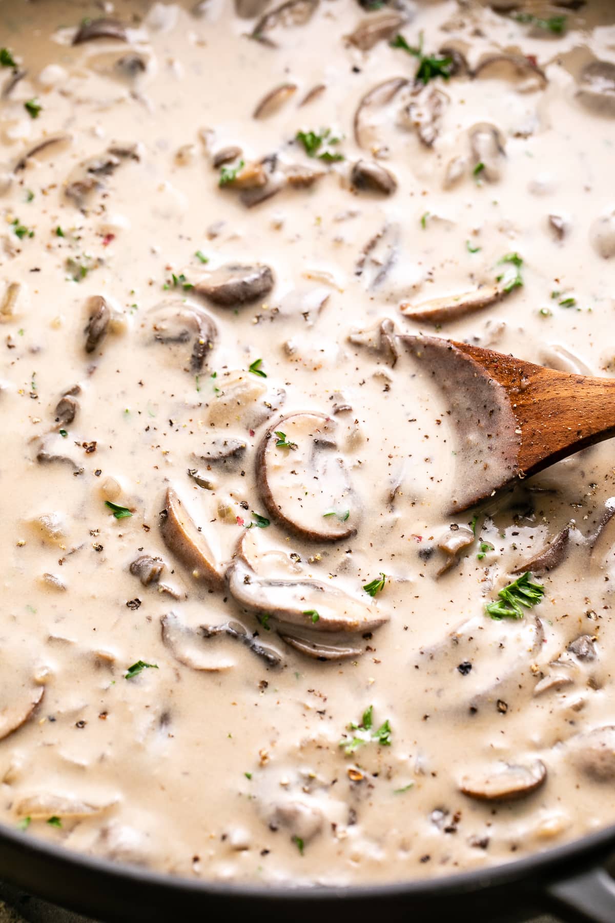 side angle view of vegan mushroom stroganoff sauce in a pan with wooden spoon.