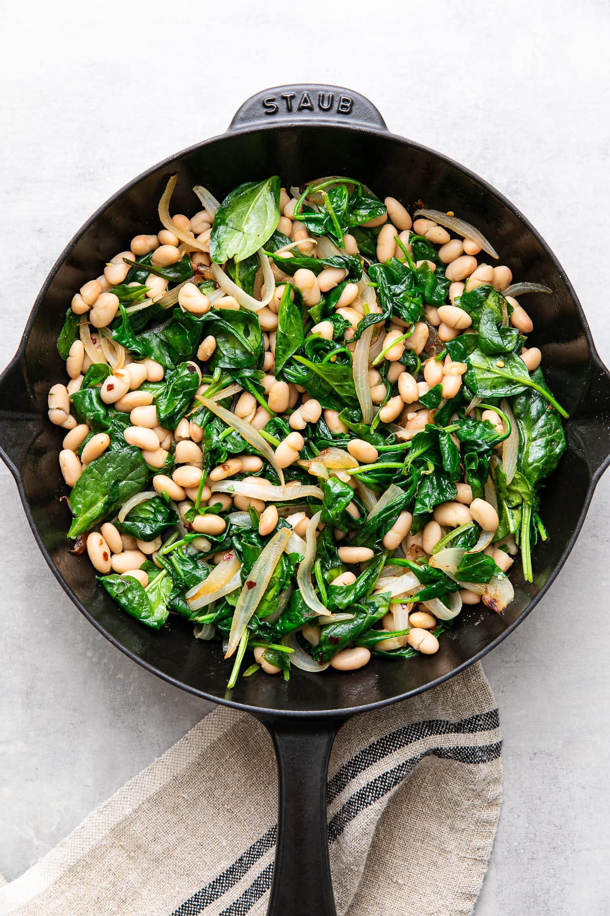 top down view of sauteed white beans and spinach in a cast iron skillet.