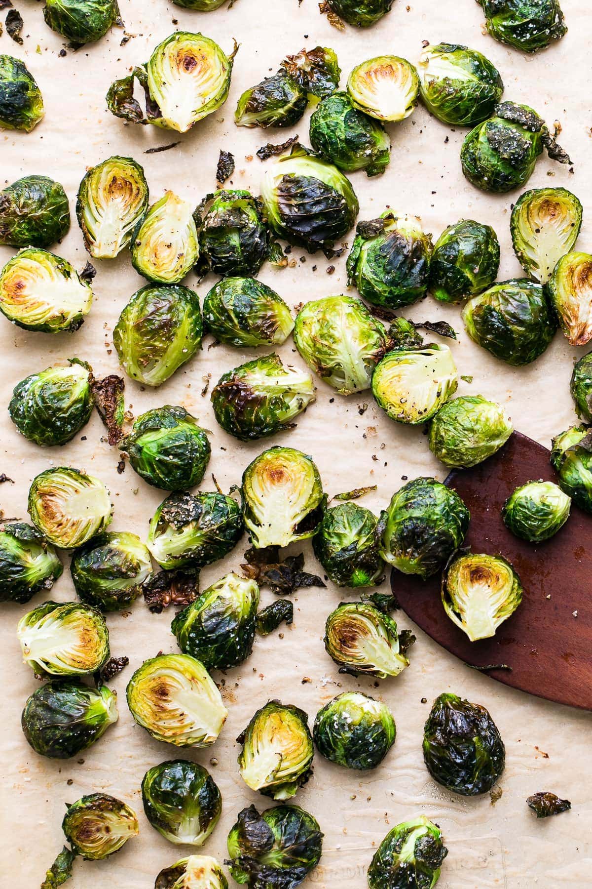 top down view of freshly roasted brussels sprouts on baking sheet with wooden spatula.
