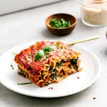 side angle view of slice of vegan lasagna on a plate with items surrounding.