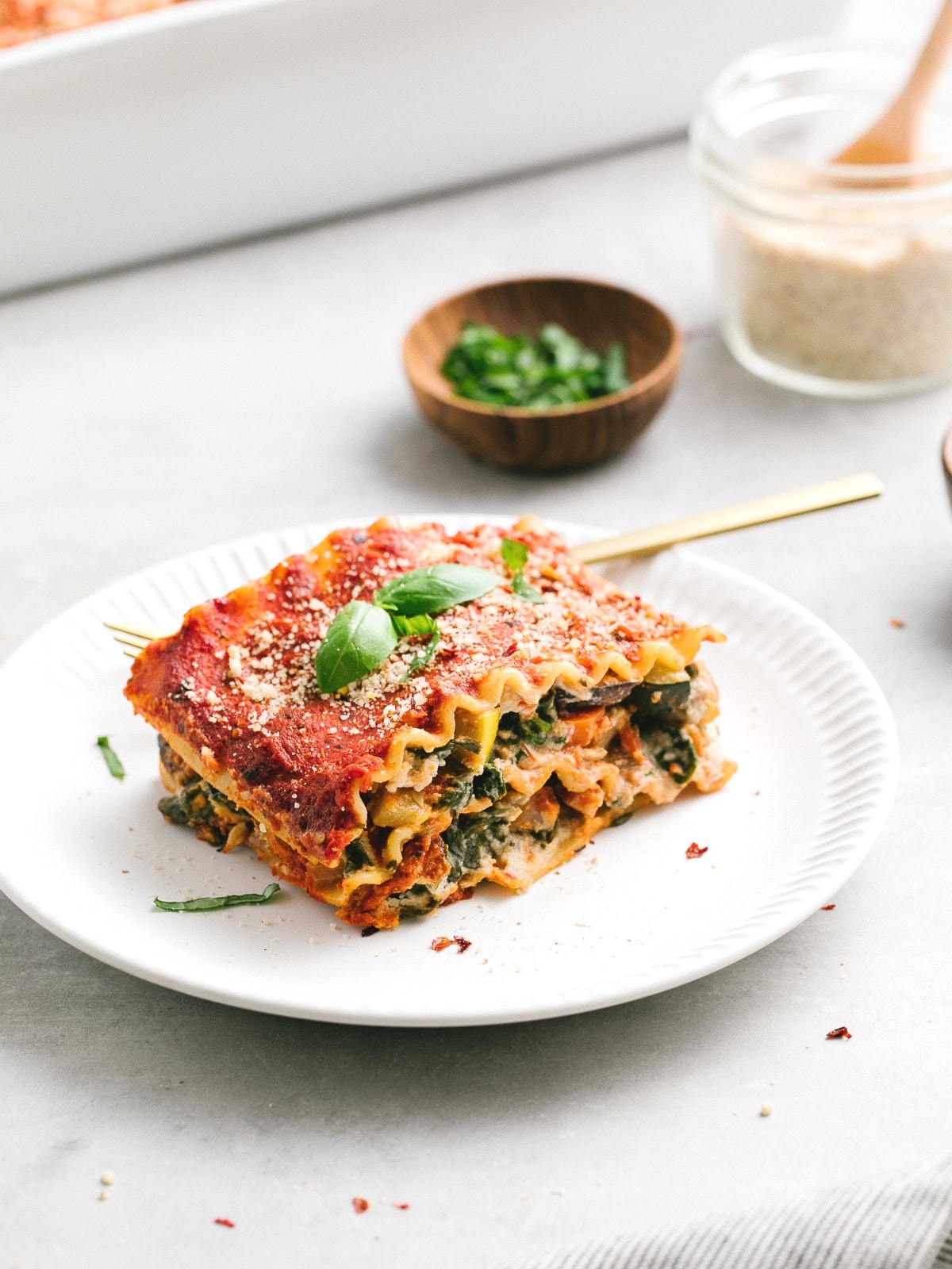 side angle view of slice of vegan lasagna on a plate with items surrounding.