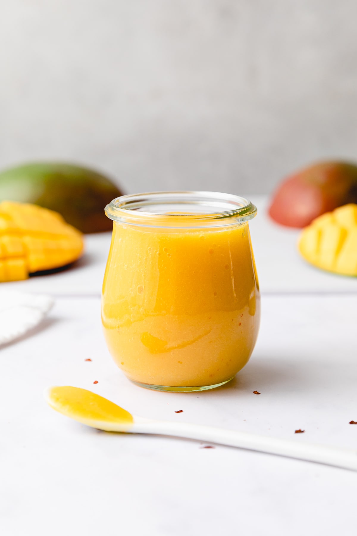 head on view of mango dressing in a glass jar with items surrounding.