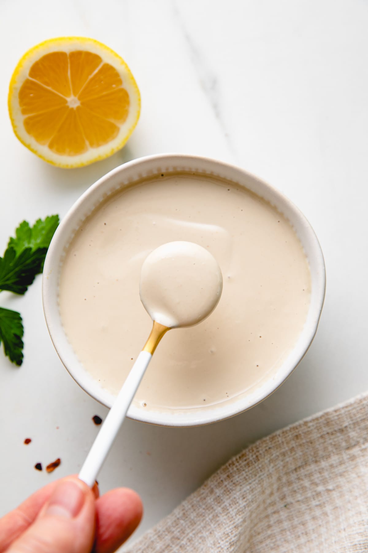 top down view of spoonful of tahini sauce over small serving bowl.