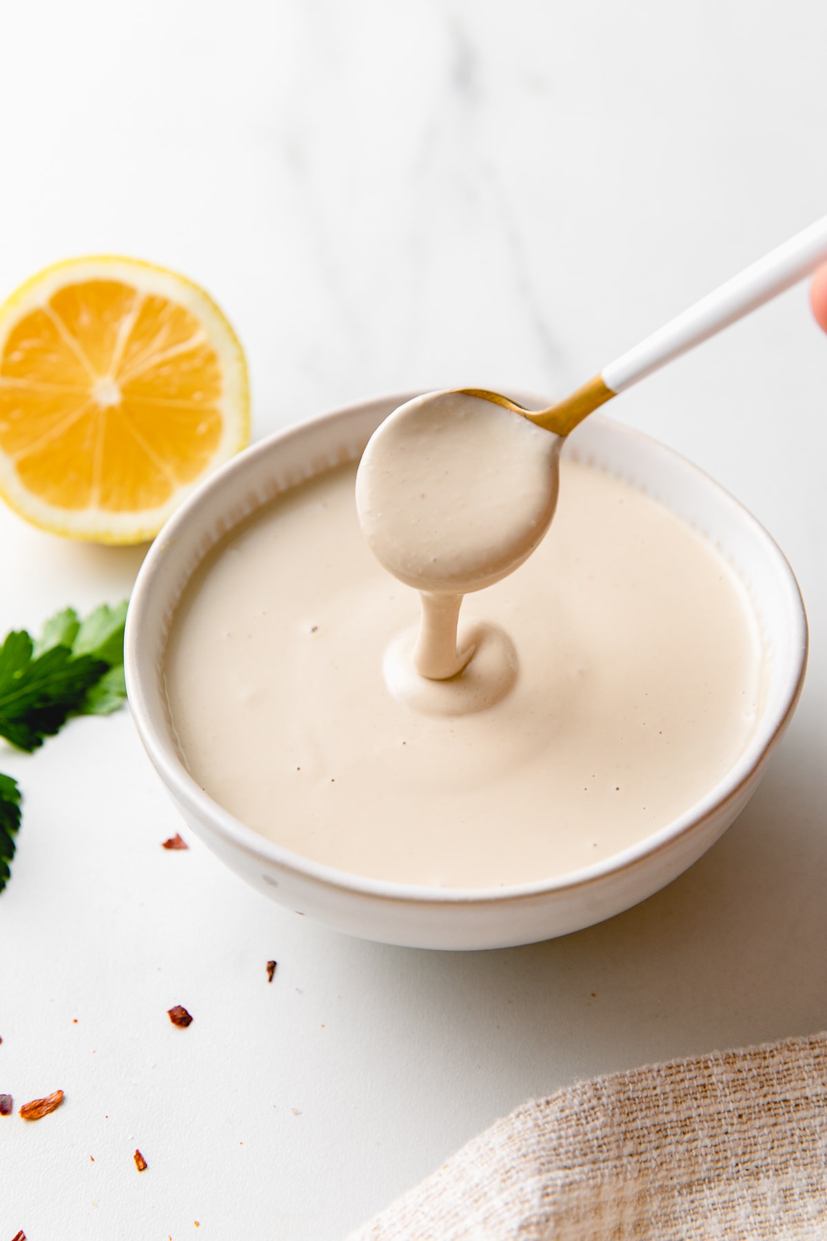 side angle view of spoonful of tahini sauce spilling into a small bowl.