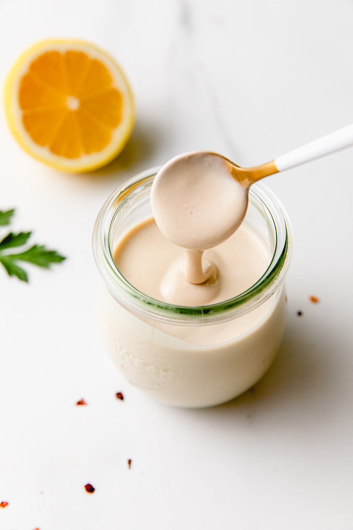 side angle view of spoonful of tahini sauce spilling into a glass jar.