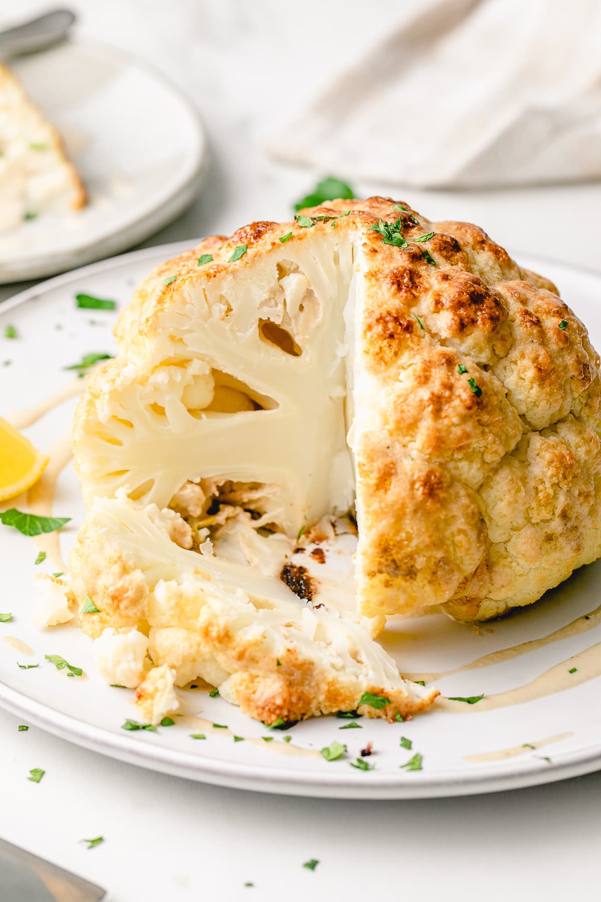 head on view of whole roasted cauliflower with slice cut on a serving platter and items surrounding.