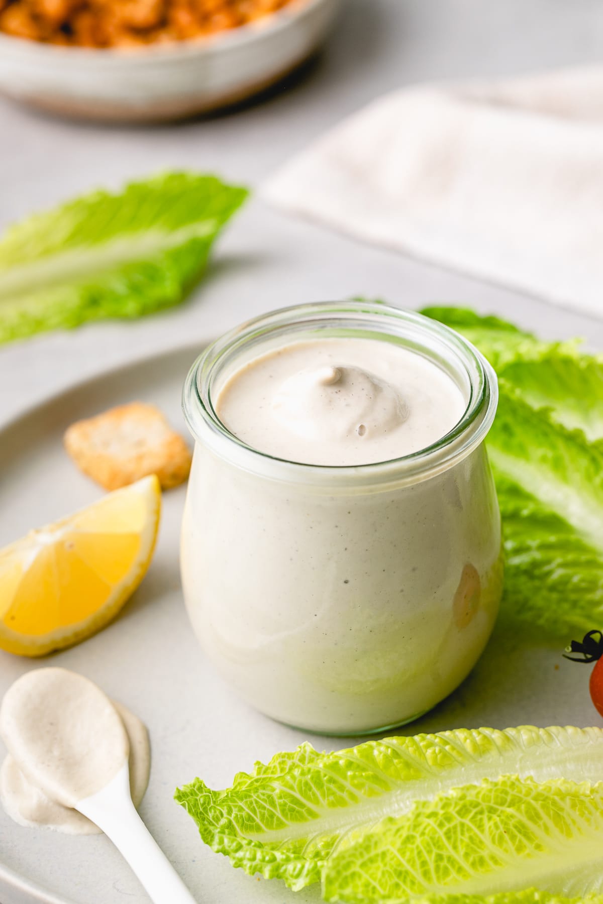 side angle view of vegan caesar dressing in a glass jar with items surrounding.