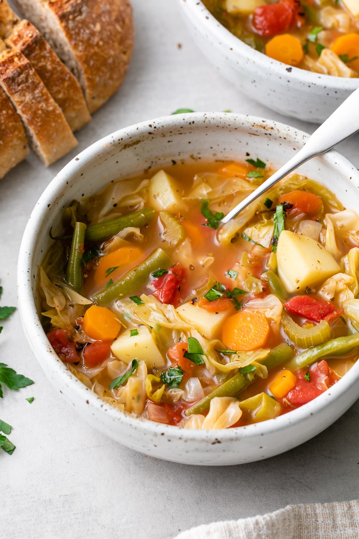 side angle view of soup bowl with vegetable cabbage soup and items surrounding.