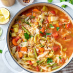 top down view of healthy vegetable cabbage soup in a pot with items surrounding.