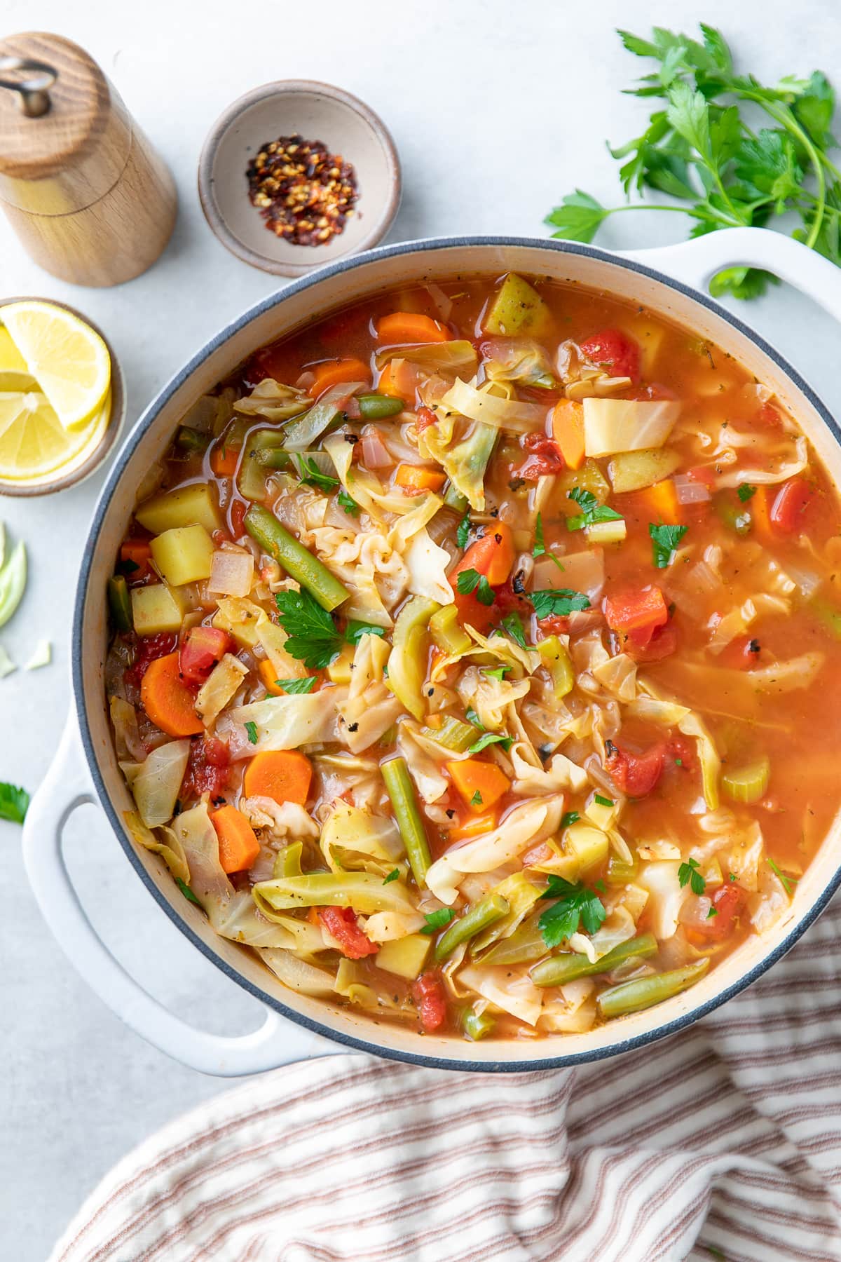 top down view of healthy vegetable cabbage soup in a pot with items surrounding.
