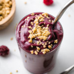 side angle view of acai smoothie with granola and items surrounding.