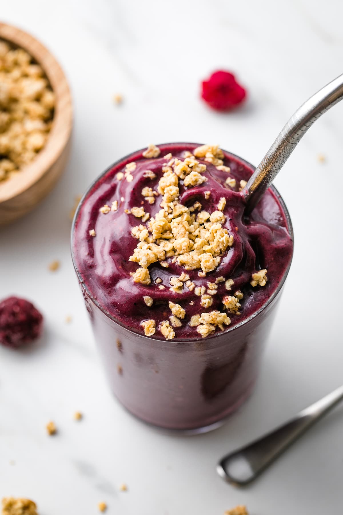 side angle view of acai smoothie in a glass with straw and granola topping.