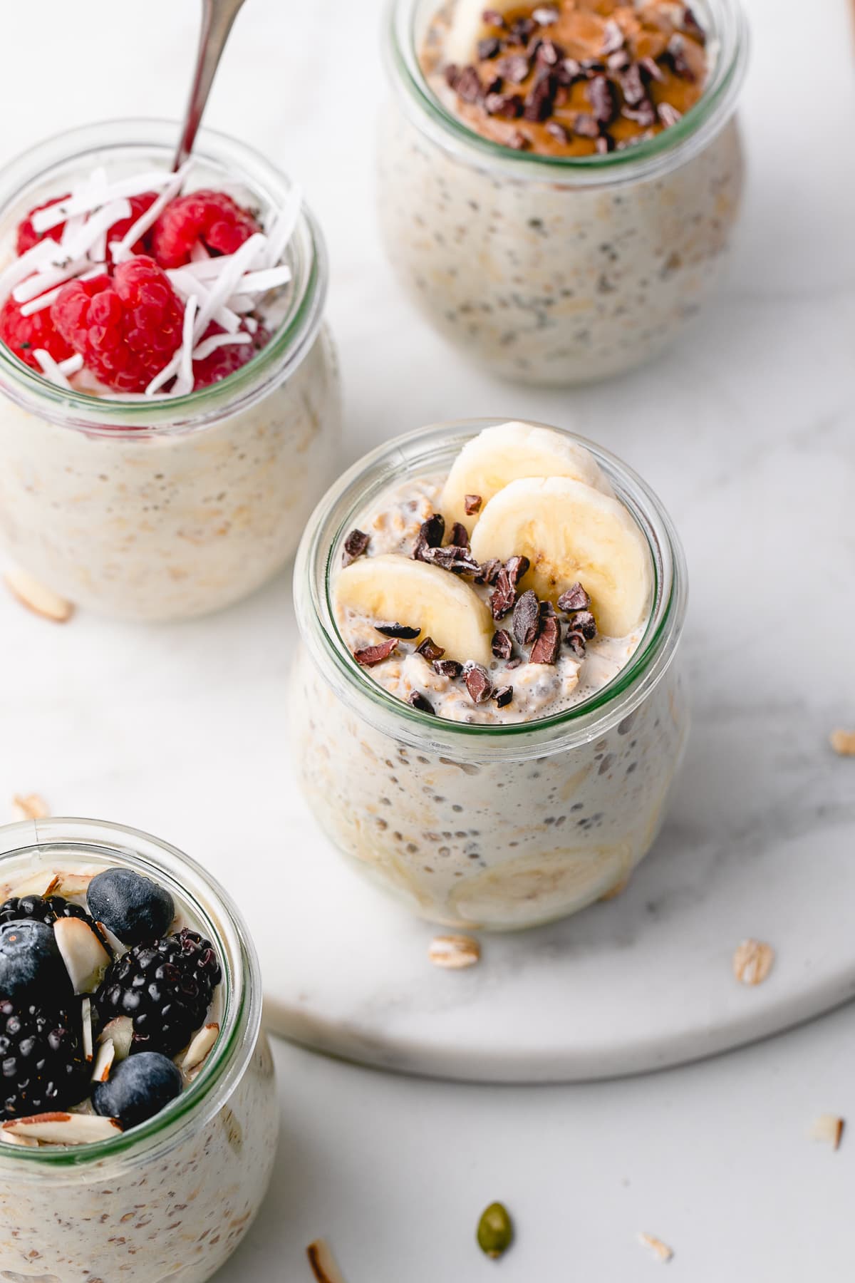 side angle view of group of healthy vegan overnight oats in glass jars with mixed toppings.
