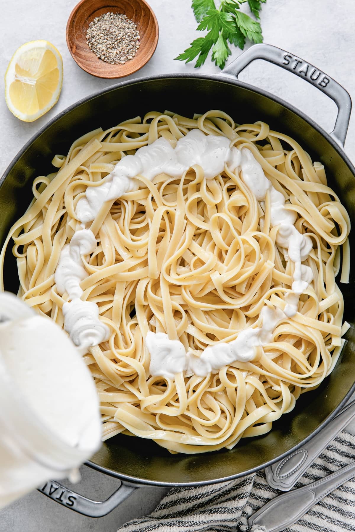 top down view of pot with fettuccini and alfredo sauce being poured overtop.