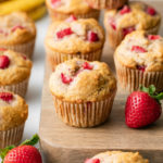 side angle view of batch of healthy strawberry banana muffins on wooden serving board.