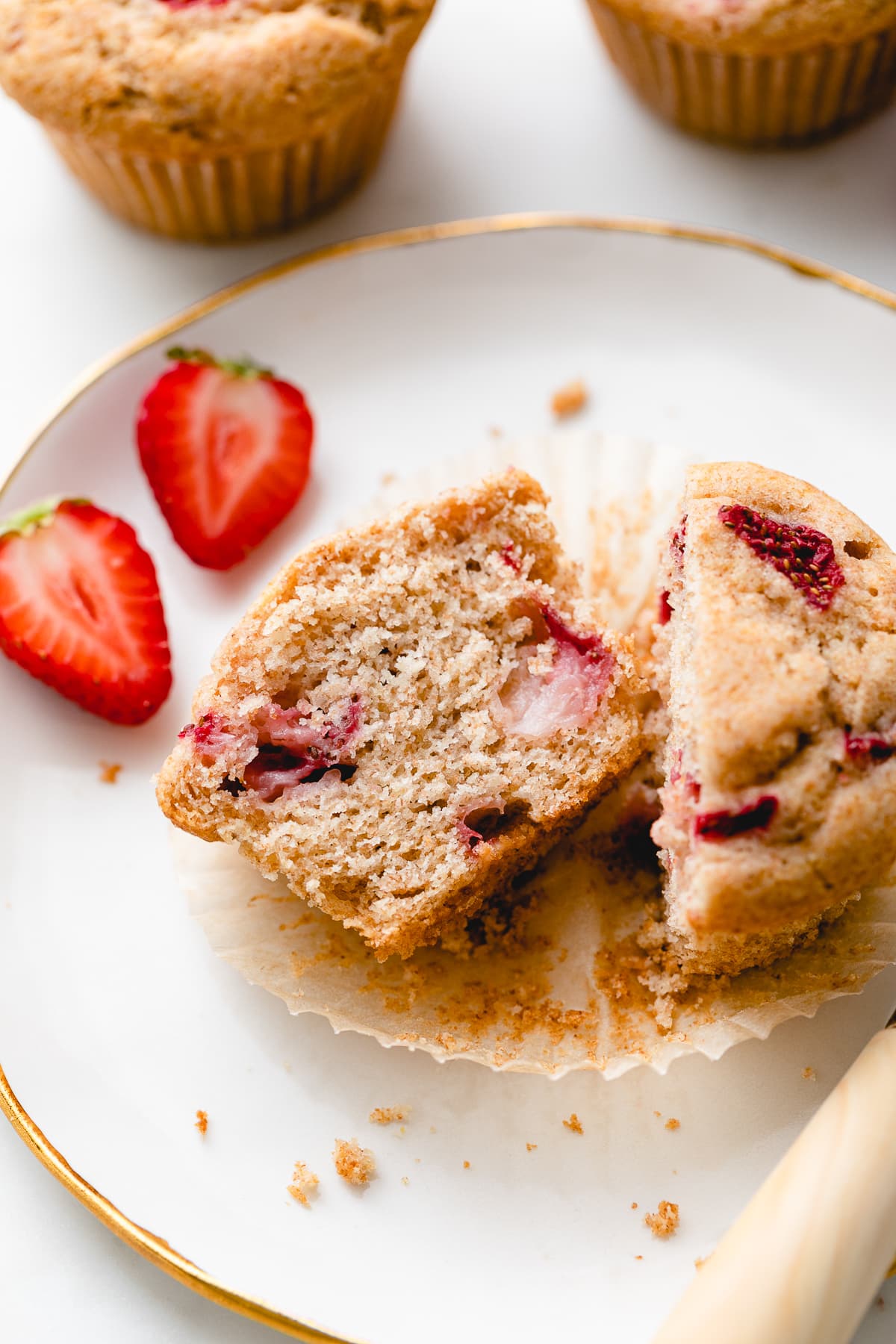 side angle view of plated strawberry muffin sliced in half with items surrounding.