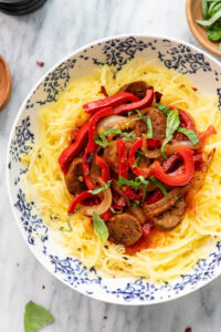 top down view of plated spaghetti squash topped with peppers, onion, and vegan Italian sausage with items surrounding.