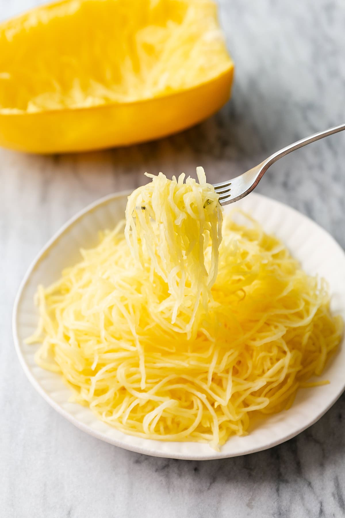 side angle view of scraped spaghetti squash flesh on a white plate with fork holding the squash to show stringiness.