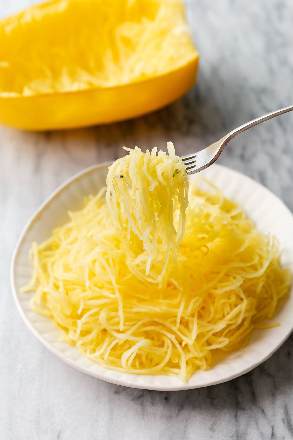 side view of plated spaghetti squash with fork holding up the stringy flesh.
