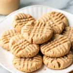 side angle view of gluten free peanut butter cookies on a white plate with items surrounding.