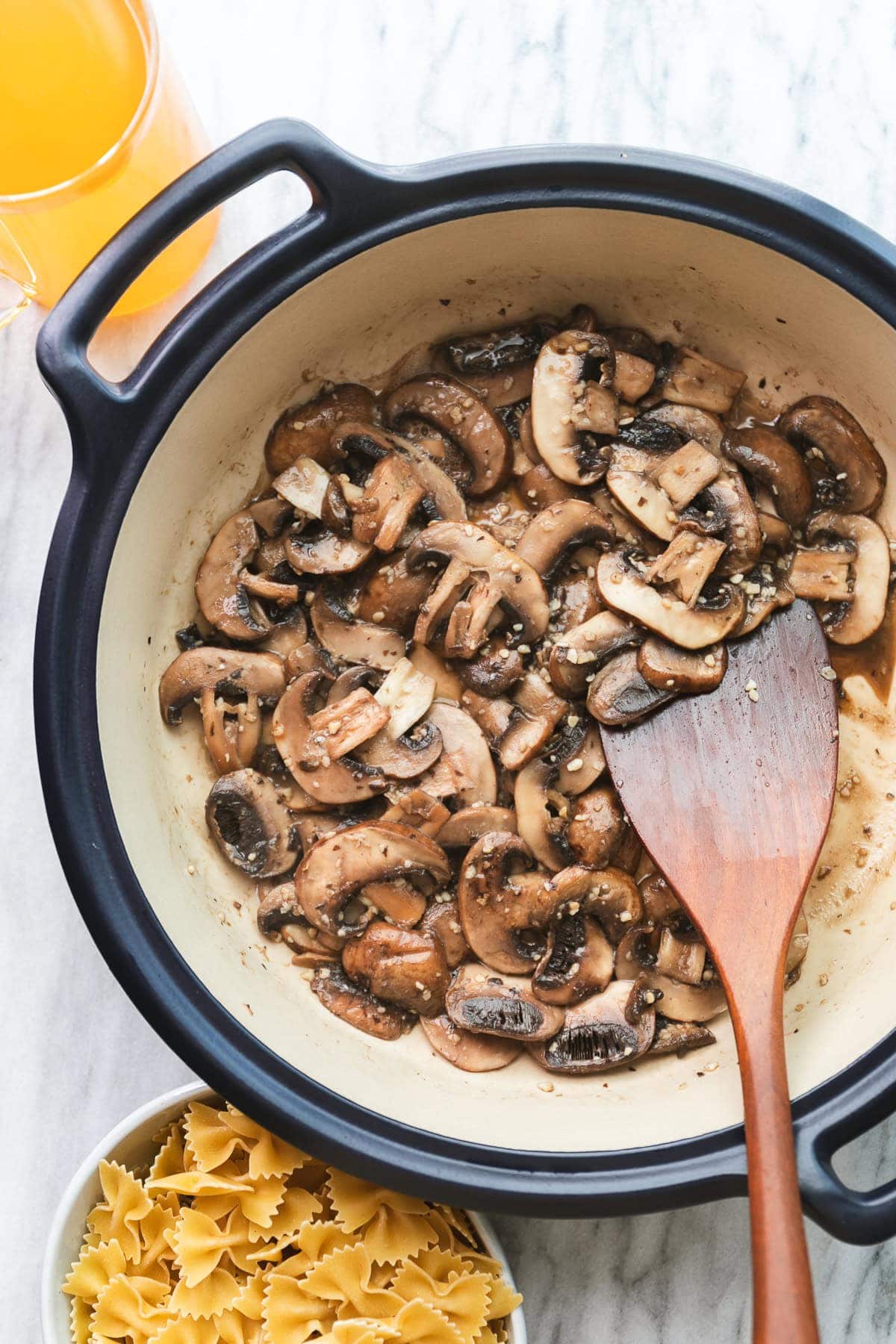 top down view of sauteed mushrooms in a pot with wooden spoon and items surrounding.