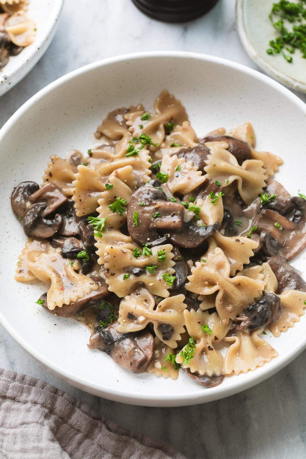side angle view of serving of mushroom pasta on a brown plate with items surrounding.