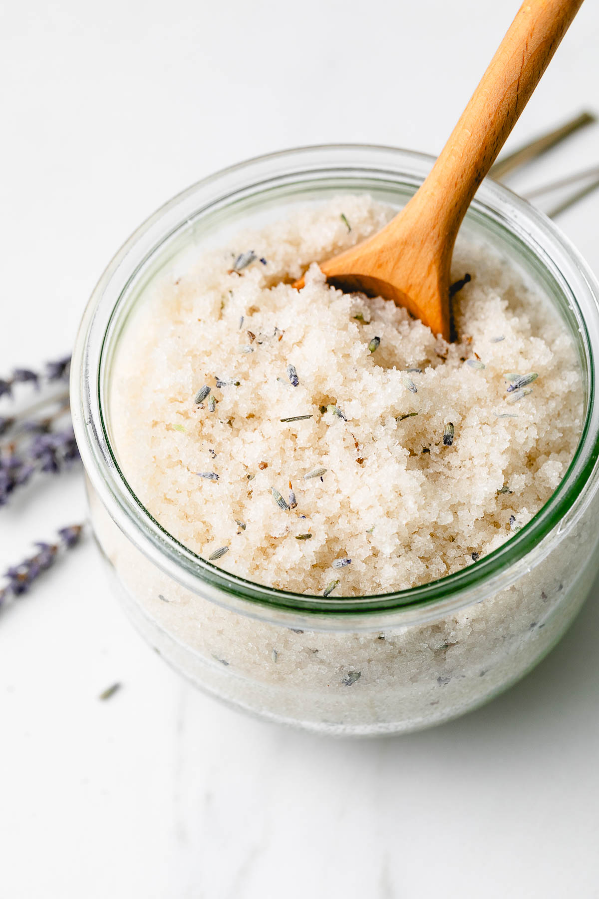 side angle view of lavender body scrub in a glass jar with wood spoon.