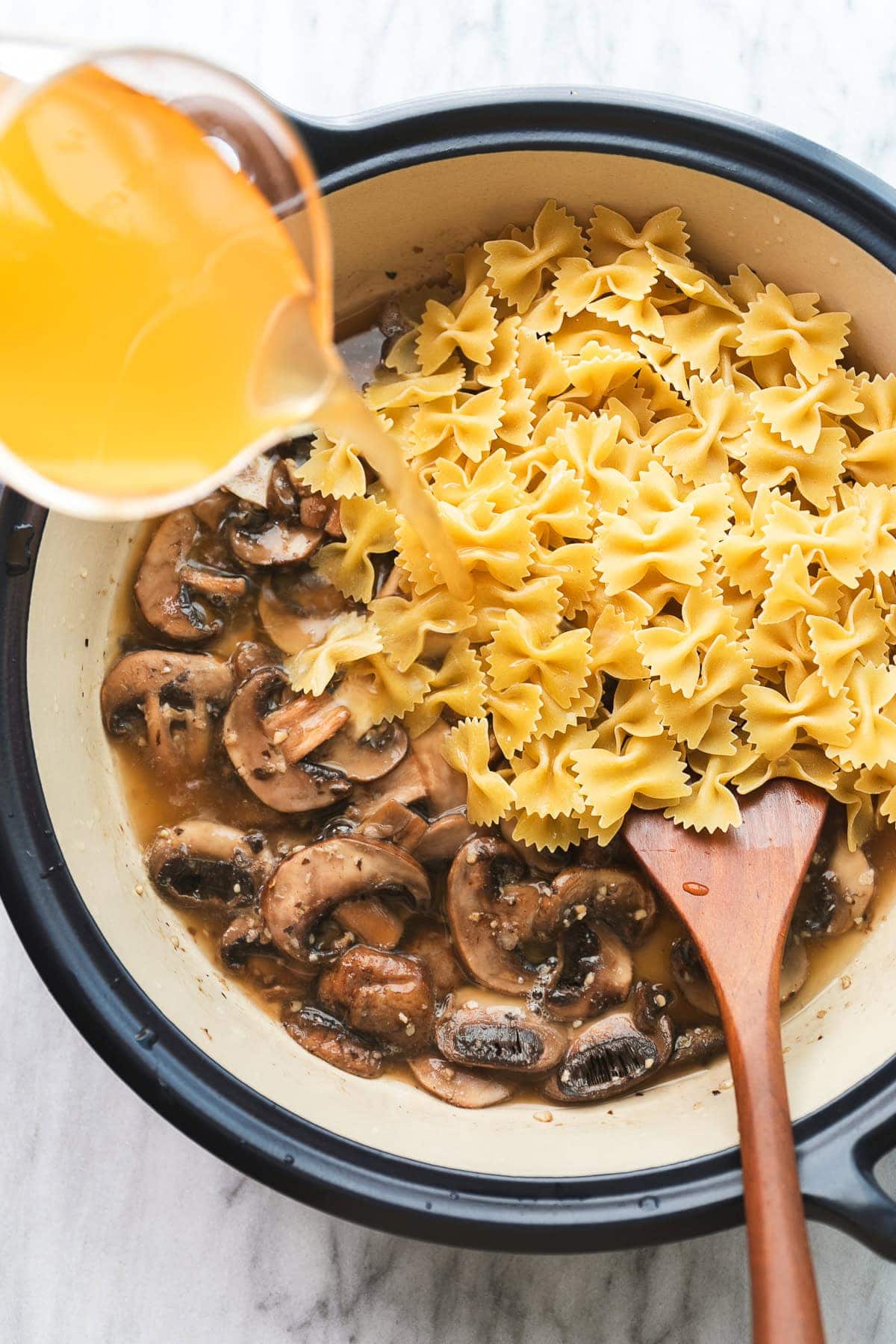 top down view of pasta and broth added to saute mushrooms in a pot with wooden spoon.