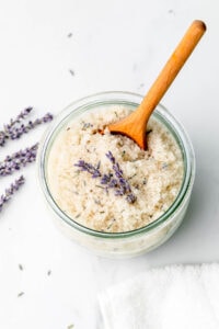 side angle view of lavender body scrub in a glass jar with wood spoon.