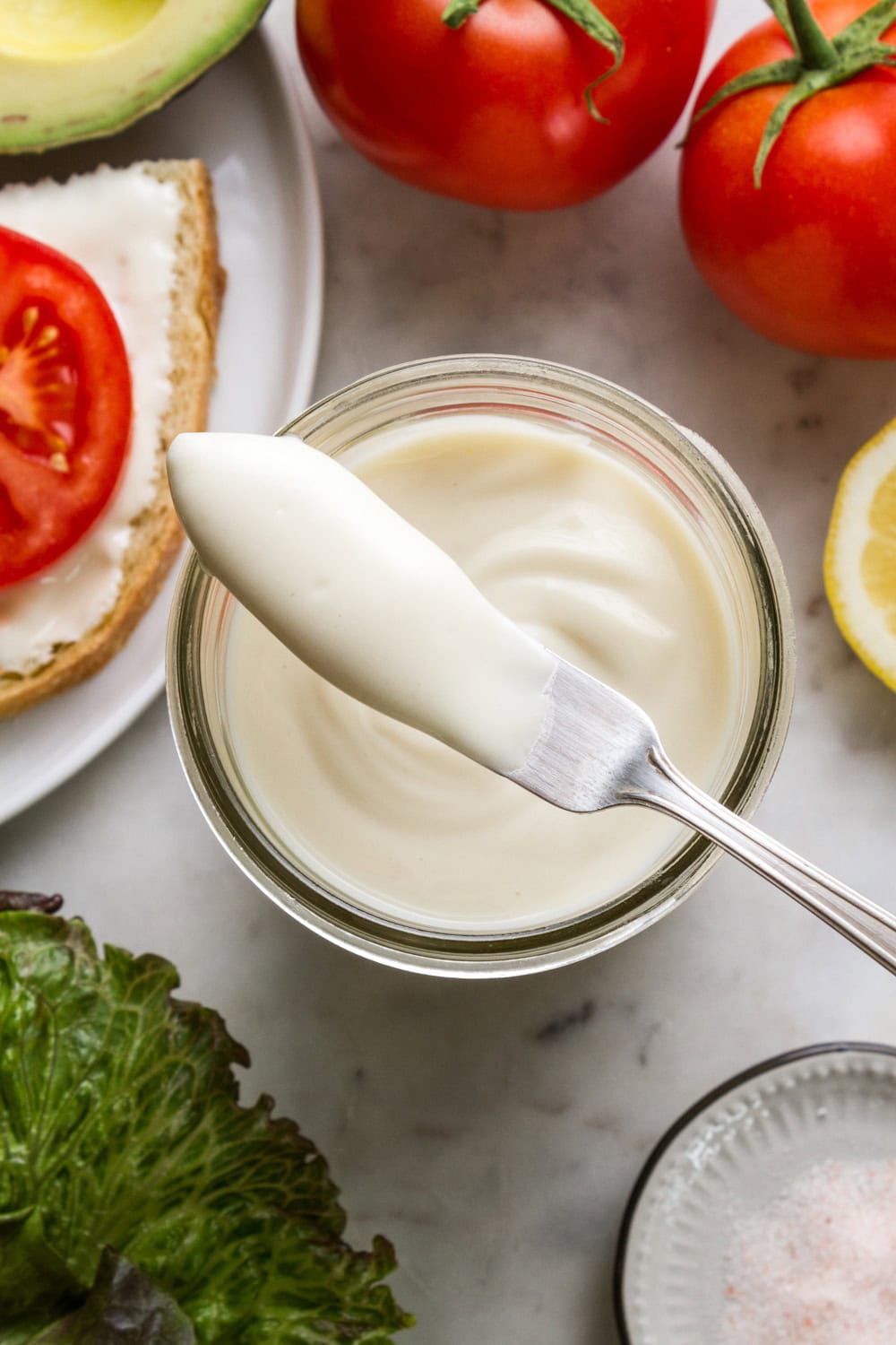 vegan mayo in a jar with butter knife and bread and veggies surrounding.