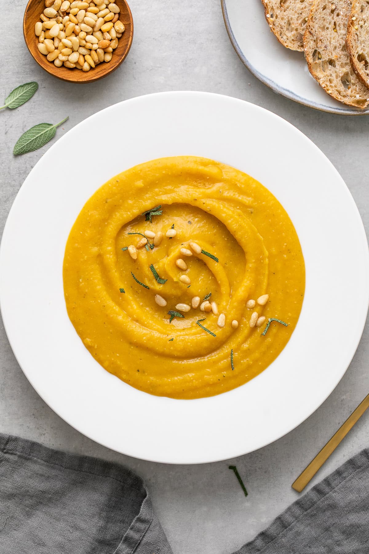 cozy vegan fall bowl with butternut squash and red lentil soup with sage and pine nut sprinkled on top.